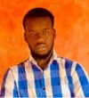 Idy Ka wearing a blue and white checkered button up, collared shirt, standing in front of a bright orange background