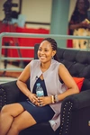 A young woman in professional attire smiling while seated in an armchair