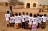 A group of young children in a line facing away towards a building in matching t-shirts with their school name