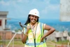 Gisele Umulisa posing with a hard hat, hammer and high visibility vest on a construction site.
