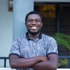 Oliver Mensah smiles in to camera wearing a patterned blue polo shirt