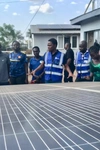 Vasco Hamisi co-founder of Okapi Green, wearing a blue vest and speaking to a group of people over a large solar panel