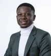Nicholas Kofi Adegbe wearing a grey blazer with a white turtleneck