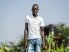 James Esinyen standing in a field in a white striped collared t-shirt and jeans