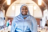 Jemila Adbulai in a light blue statin button up shirt and a light blue headscarf smiling