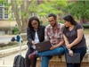 Three people sitting outside, collaborating on a laptop.