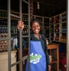 Woman standing in a shop doorway in a blue apron smiling to camera