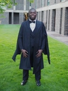 Theophilus Adu-Gyamfi smiling in his graduation cap and gown standing outdoors.