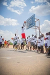 Lich Gatkoi Puok playing basketball on an outdoor court with a large group of other individuals waiting to play basketball as well.