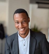 Victor Osanyindoro, Lead Finance and Operations wearing a dark grey blazer with a white collared t-shirt underneath