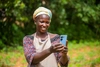 The cover page of the Social Agriculture in WAEMU report, a woman is holding a digital device outdoors and smiling in a patterned dress with a beige apron and a colourful headwrap