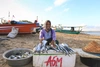 Fishmonger sits on the beach with fish in front of her