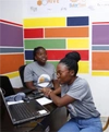 Two young women working at a desk in a room with brightly coloured wallpaper