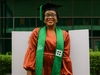 Ibukunoluwa Omotola standing in graduation cap and sash with an orange dress underneath.