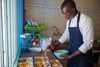 A man in an apron serving up food into trays.