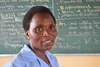   Eleder Ntamushobora smiling to camera with a blackboard in the background