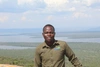 Daniel looks towards camera with a wide landscape of water and trees behind him 