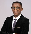 Fabrice Kwizera Rwayitare in a smart black suit, with a white collared button up shirt, and a dark purple tie with a silver tie clip