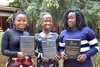 Three women stand next to each other smiling to camera holding plaques