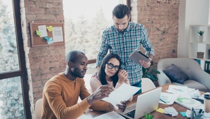 three people gathered around laptop in an office