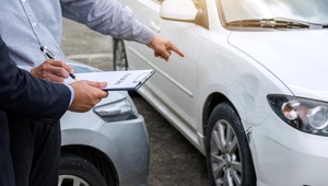 Man pointing out a dint in his car and having it assessed for insurance claim