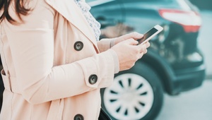 Woman using her phone in front of a parked car
