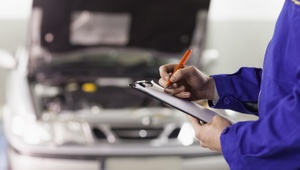 mechanic with clipboard checking car at garage 