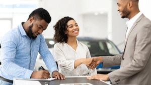 man signing car agreement and lady shaking hands with car salesman