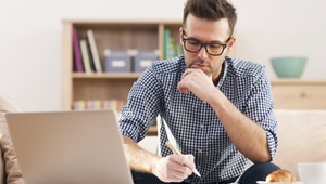 man making notes with laptop open