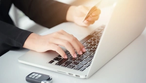 Person sat at a desk with car key entering card details into laptop 