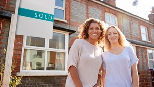 Two women stood outside the front of a house next to a sold sign