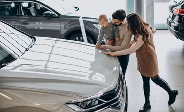 A young couple and their small child, looking at a used car in a dealership.