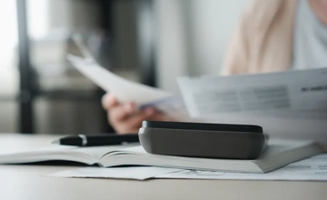 Close up image of someone looking through documents with a pen and calculator
