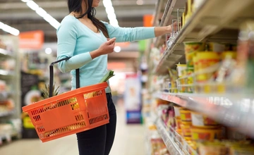 woman in supermarket holding a shopping basket and looking for cheap food items