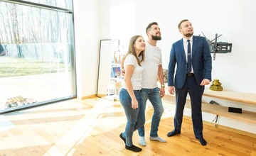 A young couple being shown around a house by a salesman.