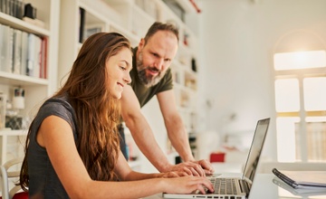 Dad and daughter both smiling and looking at their shared laptop screen.