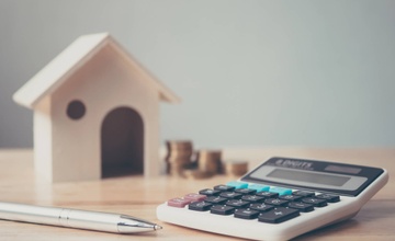 A calculator on a table with a pen and coins