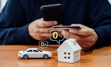 Close up of a man with his phone and credit card with a model home and a model car in front of him with 0% bubbles around the models