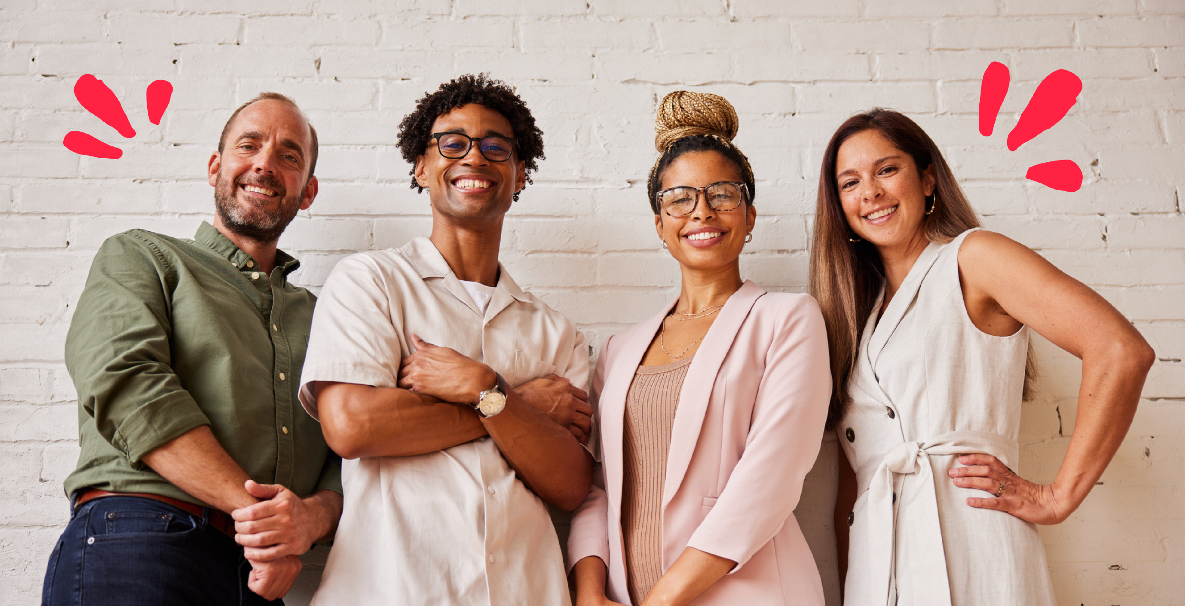 diverse group of people, two men and two women, against a brick wall, looking and smiling at camera