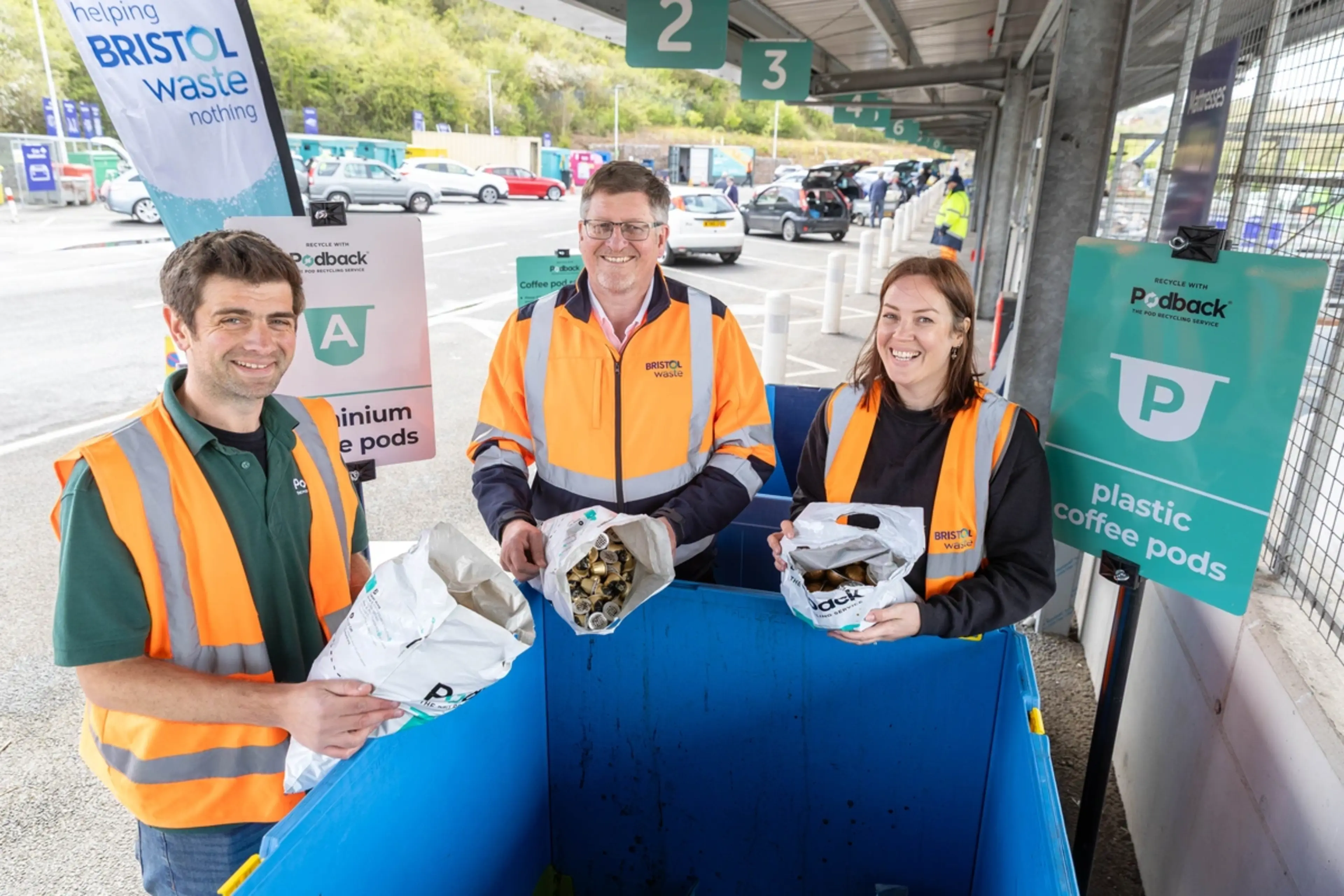 Three people in hi-vis are tipping used coffee pods into a container at a recycling centre