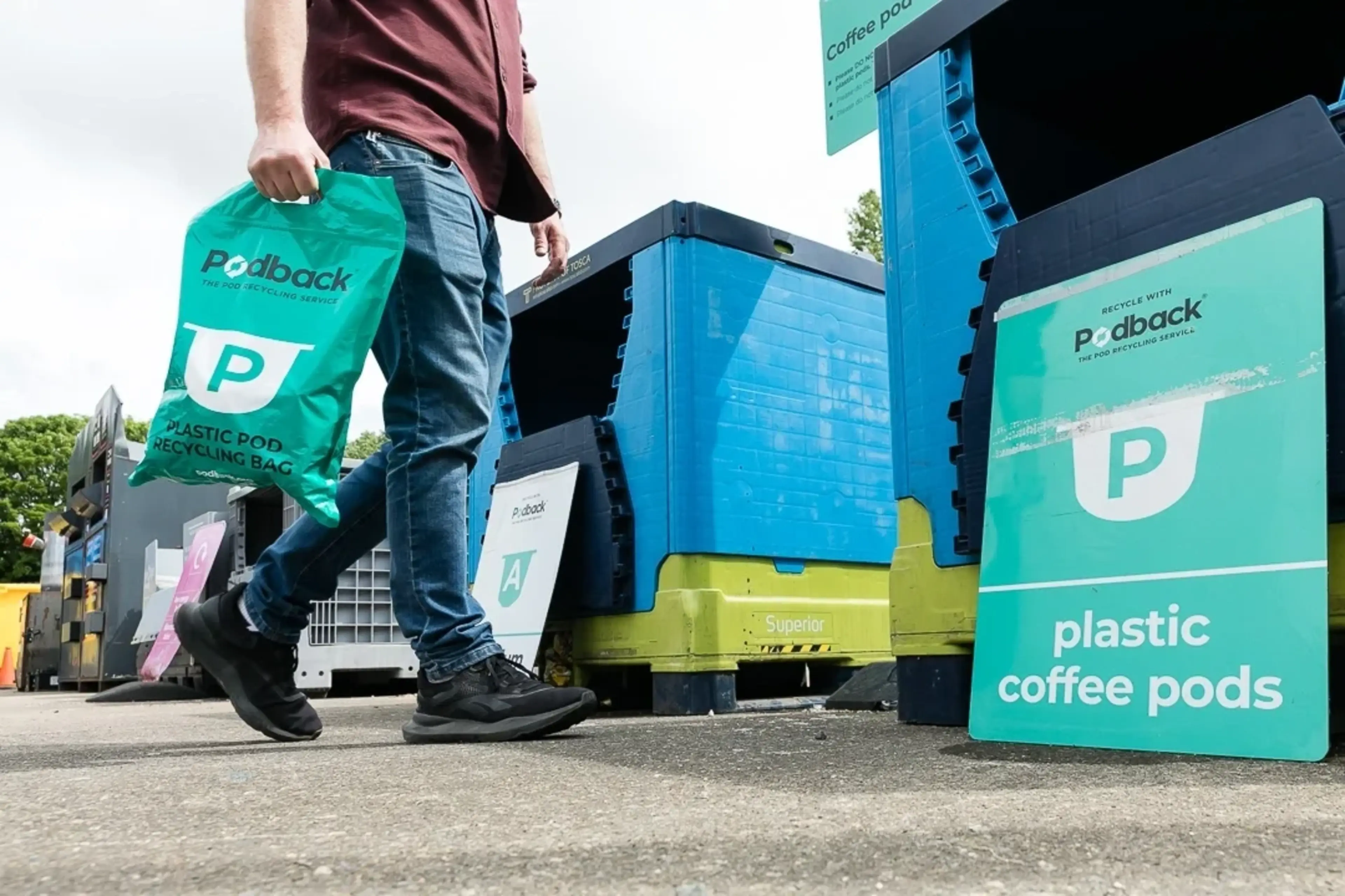A resident walks up to a recycling container with a bag of coffee pods