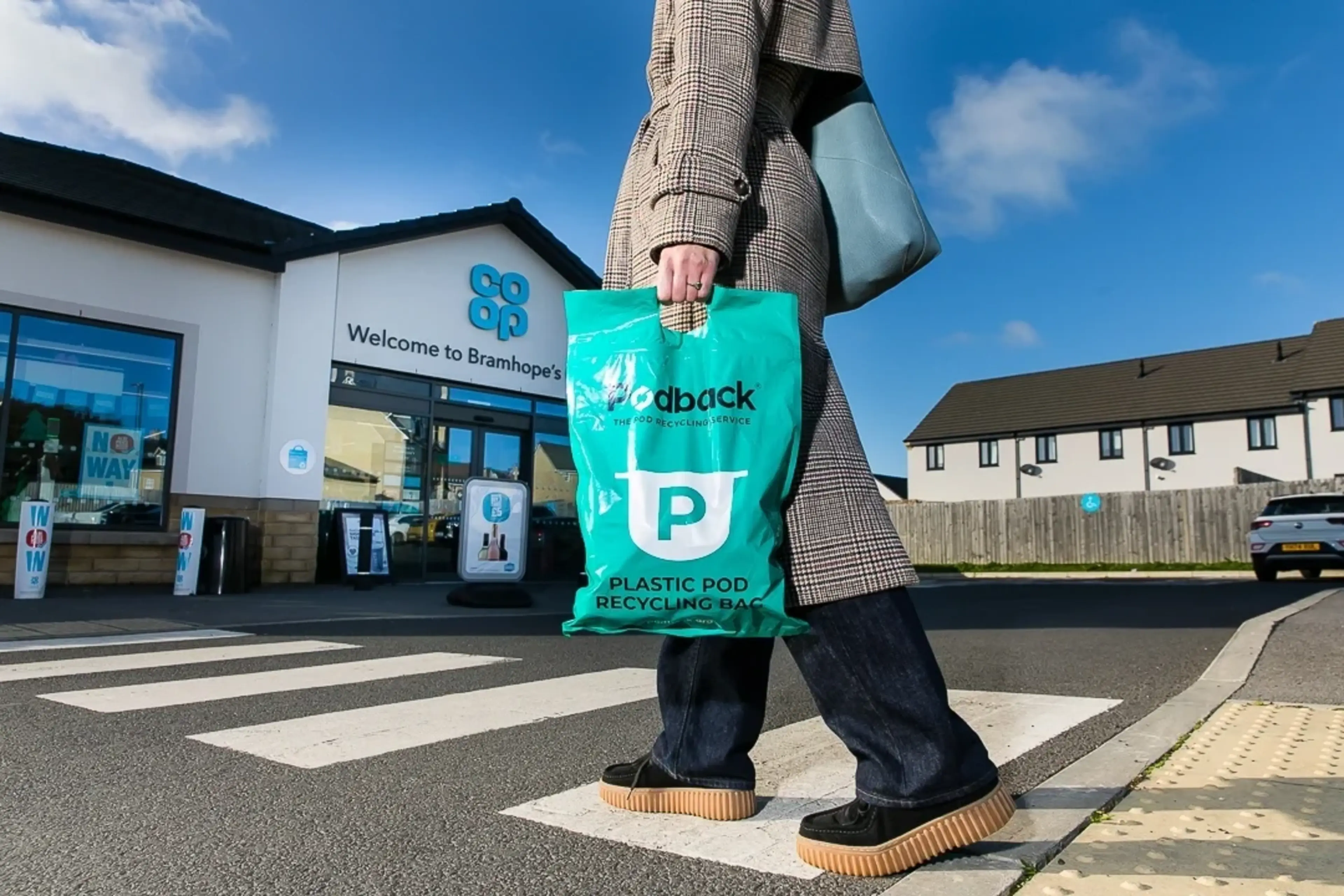 A woman carrying a Podback coffee pod recycling bag enters a Co-op store