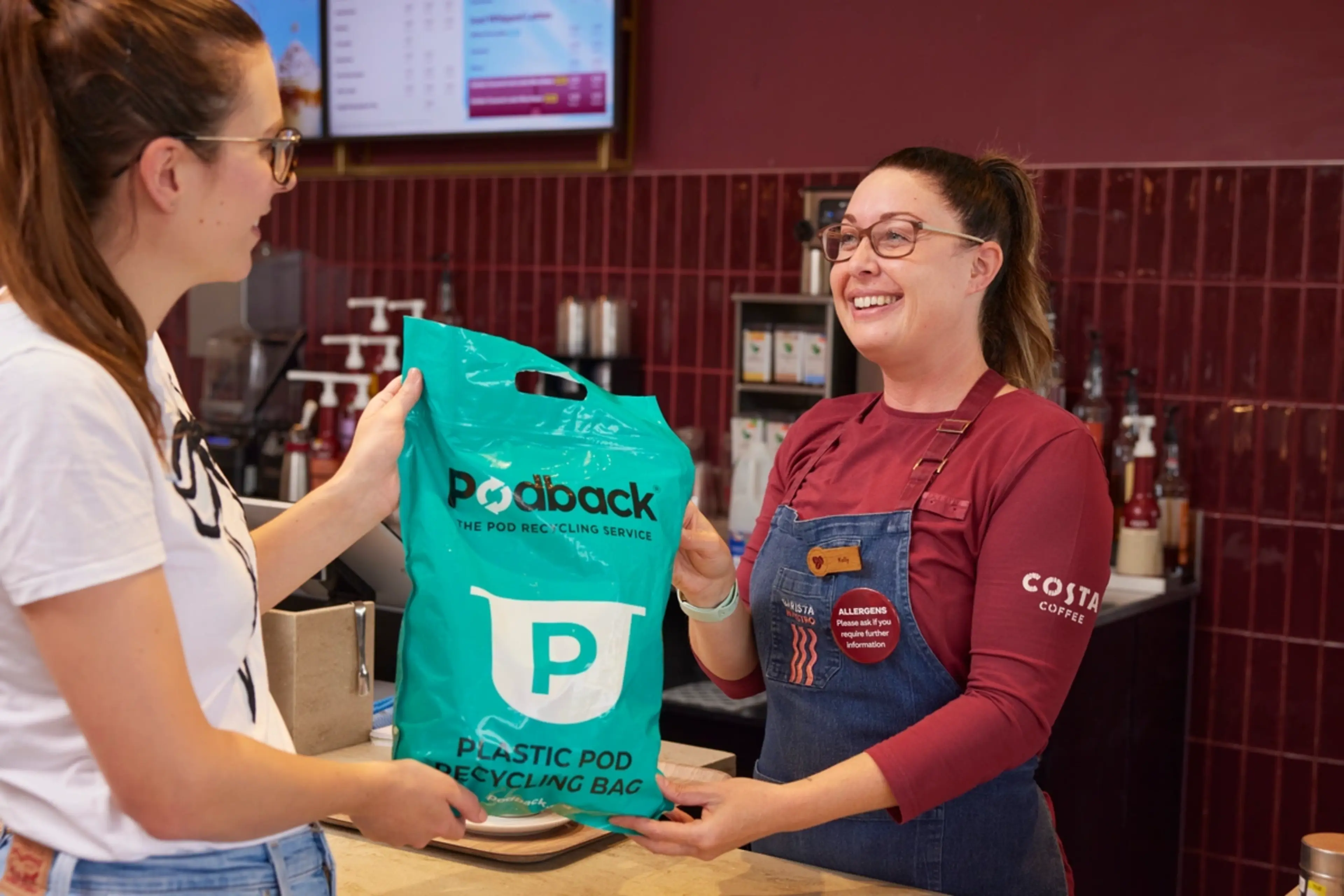 coffee shop customer handing a green Podback recycling bag to a Costa Coffee barista