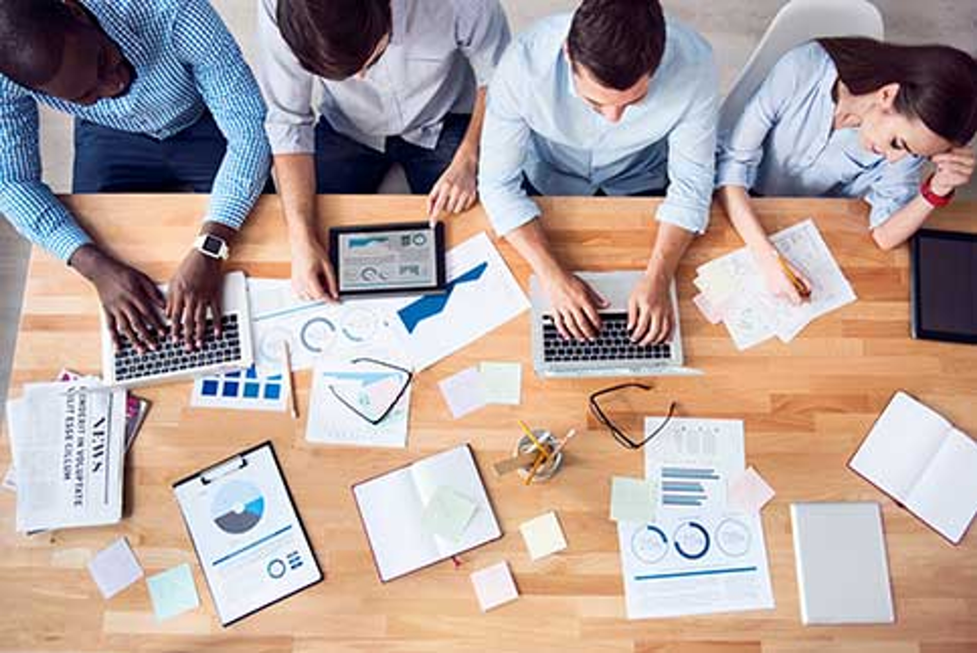 Overhead view of four people sitting at one desk with scattered papers