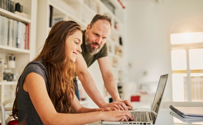 Dad and daughter both smiling and looking at their shared laptop screen.