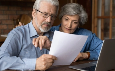 Older couple looking over a document with their laptop open