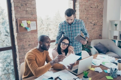 three people gathered around laptop in an office