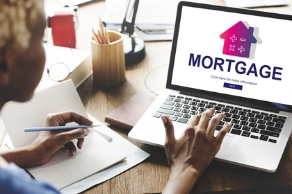 A woman sits using a laptop. On the screen there's a picture of a house in a pink to purple gradient, and the word mortgage in all caps.