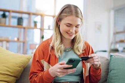 woman sat on her phone and holding her credit card
