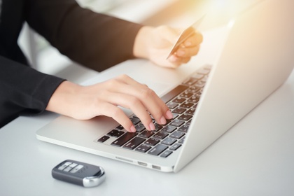Person sat at a desk with car key entering card details into laptop 